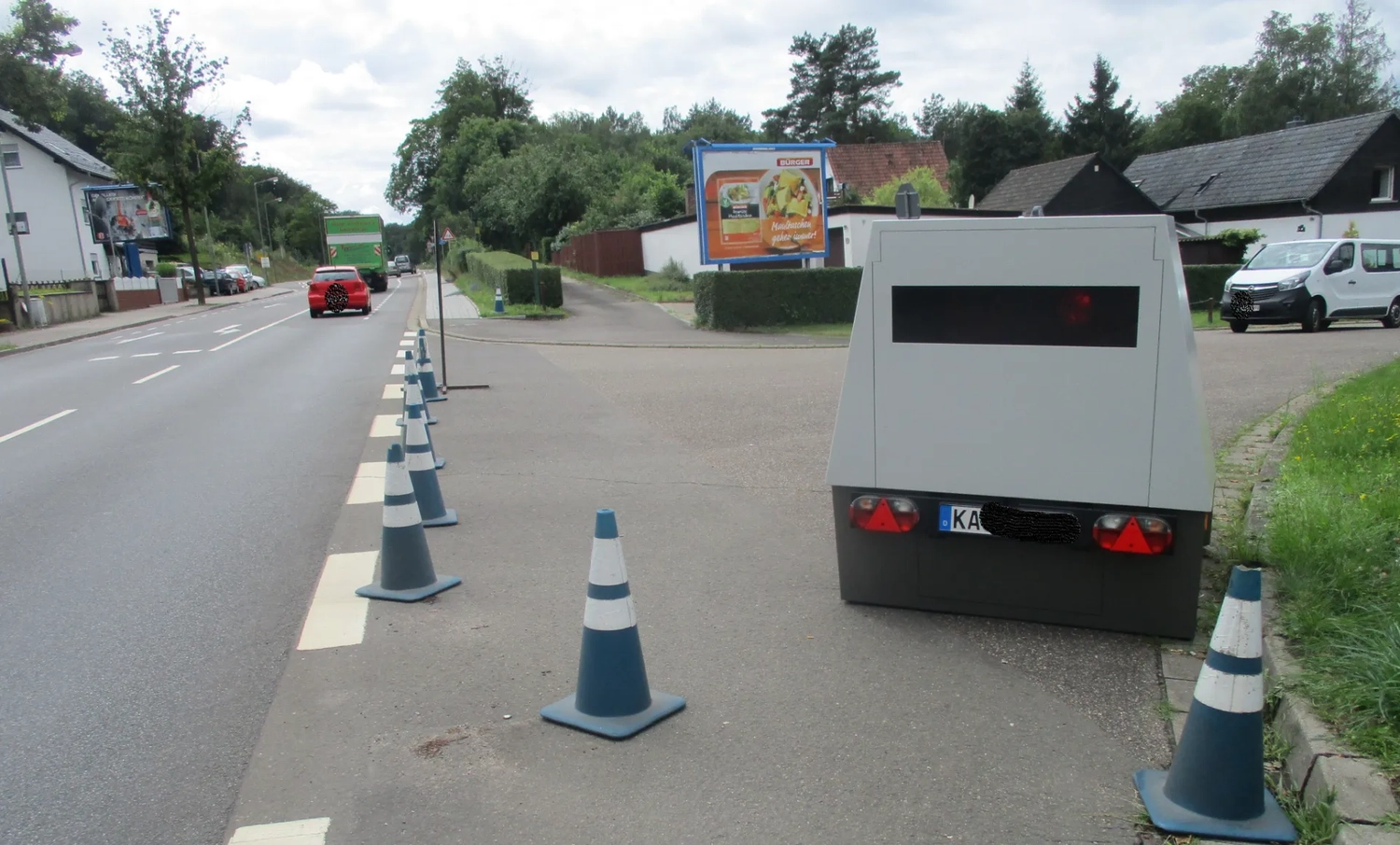 Radarrent GmbH – Verkehrsüberwachung – Geschwindigkeitsradar-Anhänger parkt auf einer Seitenstraße neben einer Reihe blauer und weißer Verkehrskegel an einer Vorstadtstraße