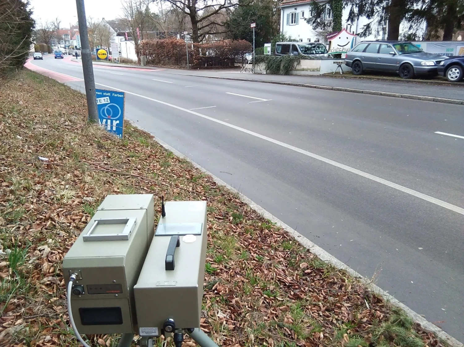 Radarrent GmbH – Verkehrsüberwachung – Zwei graue Verkehrsüberwachungsgeräte auf Stativen an einer Vorstadtstraße mit geparkten Autos und Häusern im Hintergrund