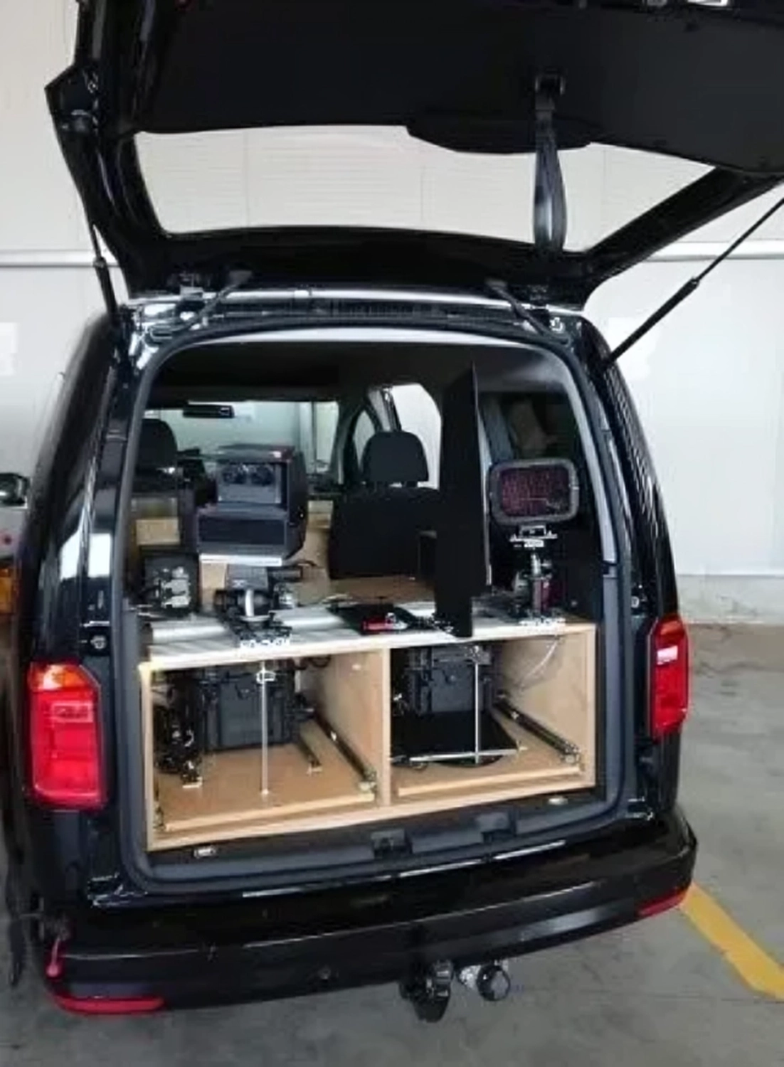 Radarrent GmbH – Verkehrsüberwachung – Offener Heckbereich eines schwarzen Transporters mit einem maßgefertigten Holzregal, in dem elektronische Geräte und Vorrichtungen montiert sind